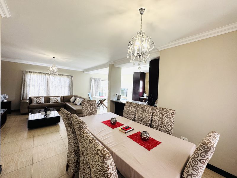 Spacious open-plan living and dining area featuring tiled floors, elegant crown molding, and crystal chandeliers, seamlessly connecting to a functional kitchen space.