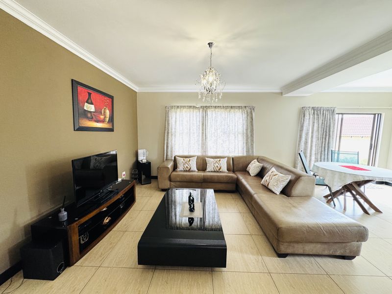 Spacious open-plan living and dining area featuring neutral tiled flooring, crown molding, and a decorative crystal chandelier, with access to an outdoor patio.