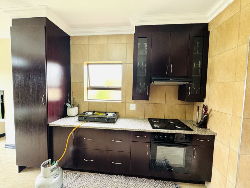 A functional kitchen featuring dark wood cabinetry, granite countertops, built-in oven, and a combination of electric and gas hobs with tiled splashbacks.