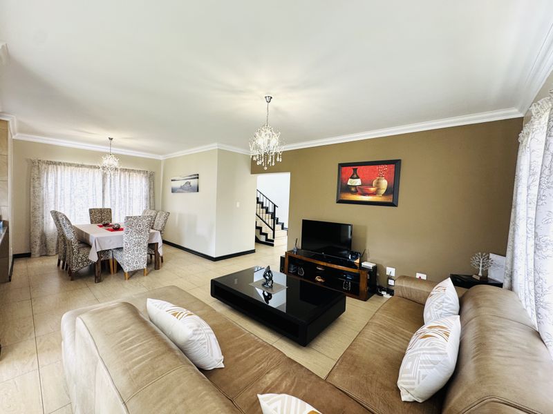 Spacious open-plan living and dining area featuring tiled floors, elegant crystal chandeliers, and neutral wall tones, providing a comfortable and functional layout.