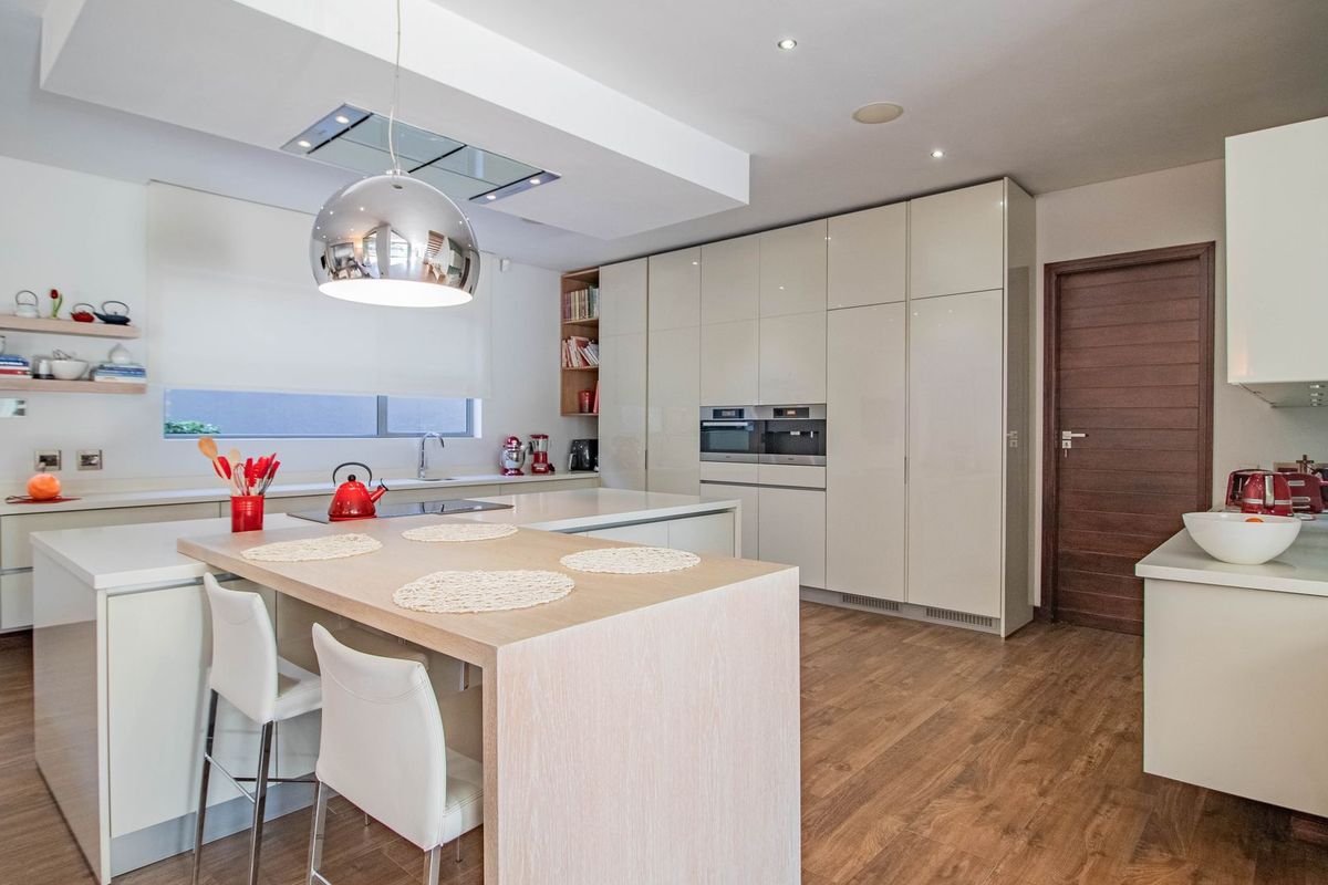 Modern, high-end kitchen featuring sleek handleless cabinetry, a central island with breakfast bar, integrated appliances, and warm wood-look flooring.