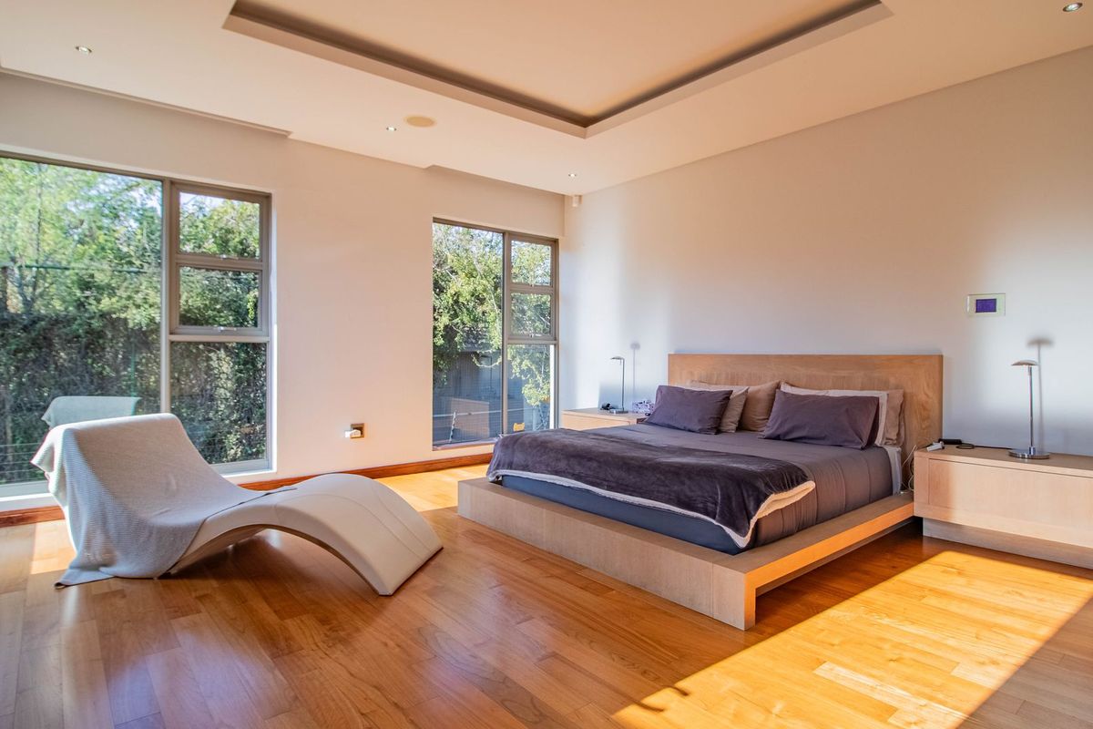 Spacious bedroom featuring warm hardwood flooring, a modern recessed ceiling design, and large windows providing ample natural light and garden views.