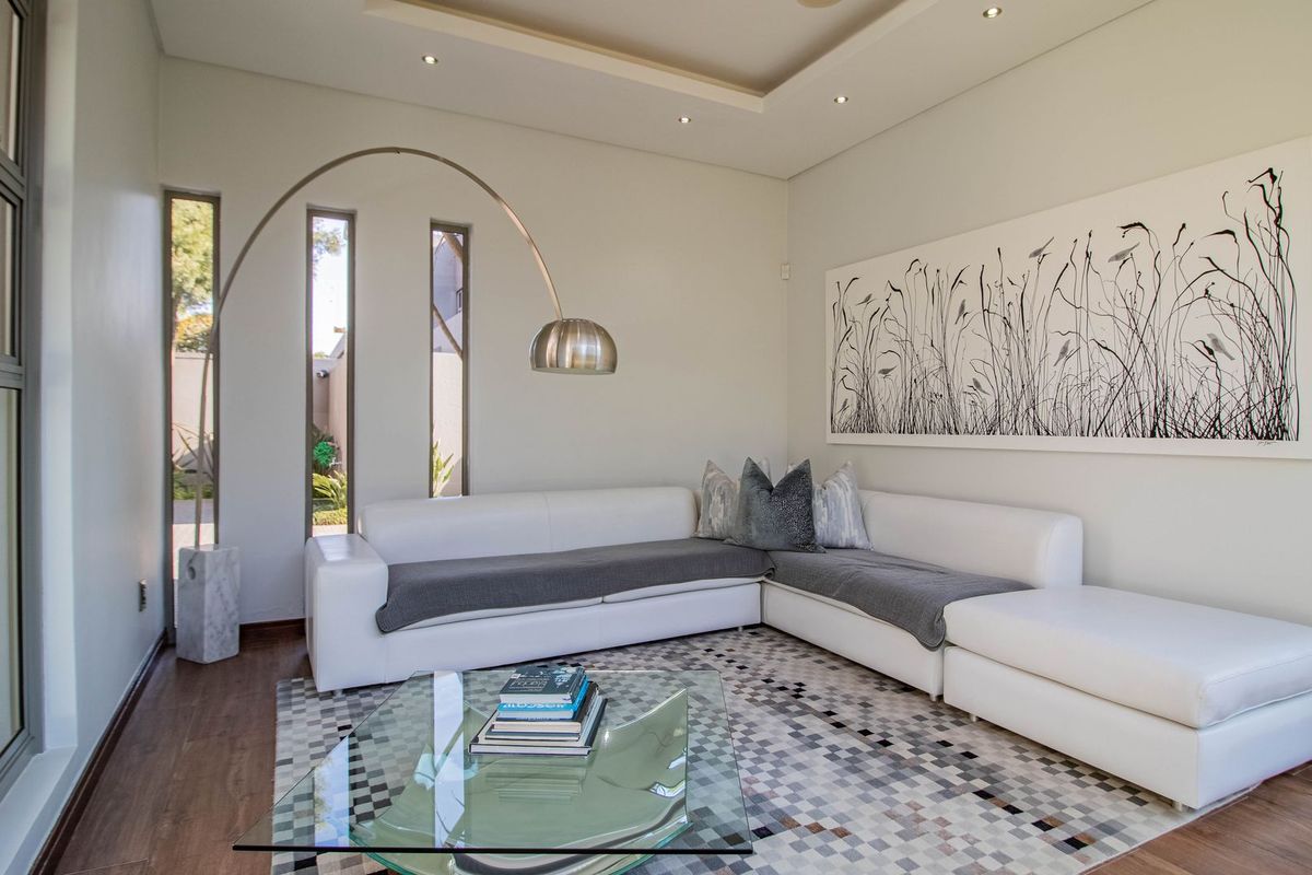 A modern, well-maintained living room featuring recessed ceiling lighting, laminate flooring, and large aluminium-framed windows that provide ample natural light.