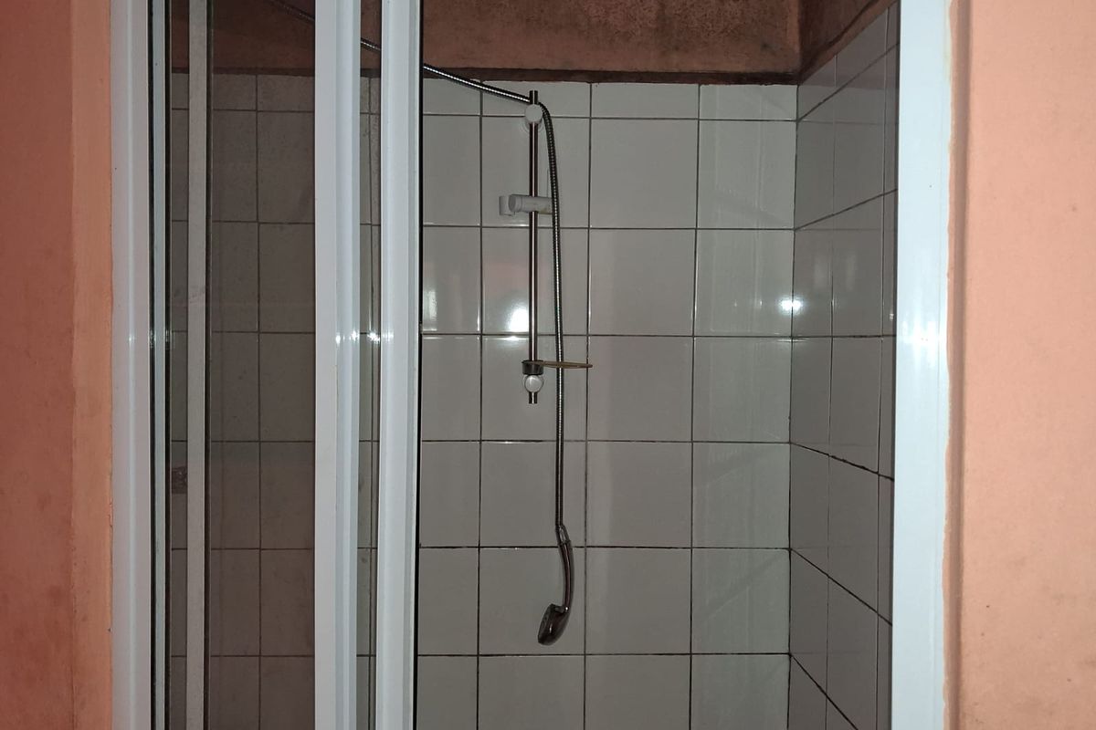 A compact shower enclosure featuring white wall tiles, a modern handheld shower fixture, and a white-framed sliding glass door.