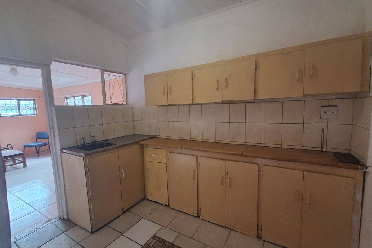 A dated kitchen featuring original cabinetry, tiled splashbacks, and a single basin sink, offering a functional layout ready for modernization.