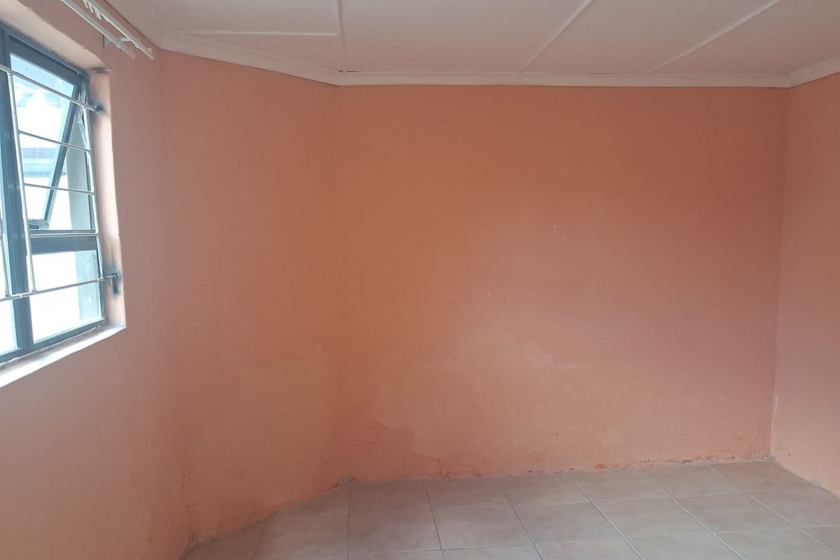 An empty bedroom featuring tiled flooring and a single window with security bars, requiring cosmetic updates to the wall finishes.