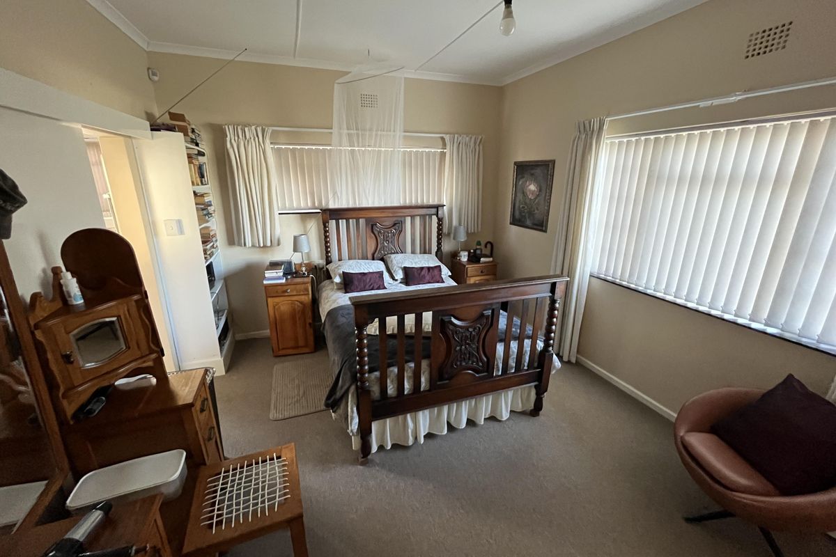 A spacious bedroom featuring neutral walls, carpeted flooring, and large windows with vertical blinds, offering a comfortable and functional living space.