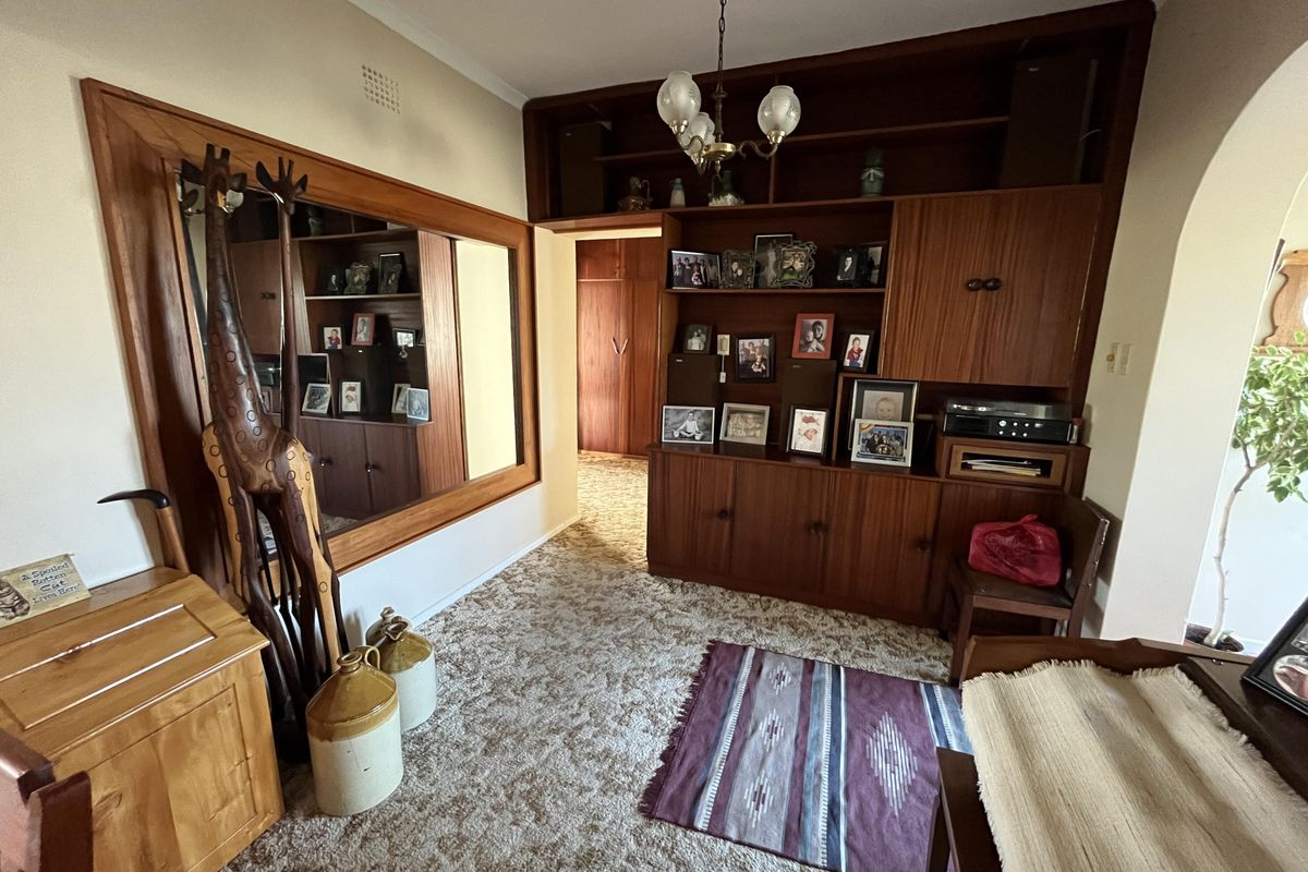 A living area featuring extensive built-in wooden cabinetry, integrated shelving, and a large wall-mounted mirror, finished with dated carpeting.