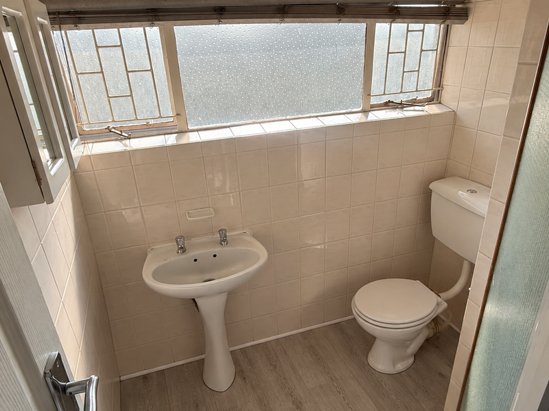A compact bathroom featuring a pedestal basin, toilet, neutral wall tiling, and wood-look laminate flooring.