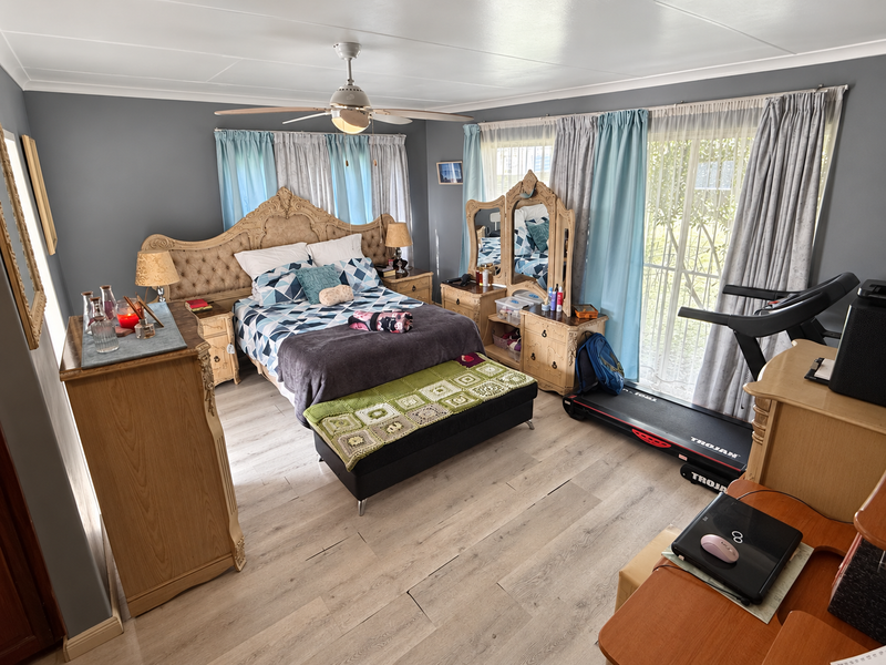 Spacious bedroom featuring light-toned laminate flooring, a ceiling fan, and large sliding glass doors that provide natural light and access to the exterior.
