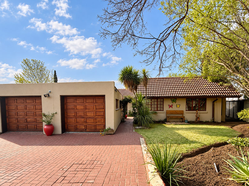 Front view of a well-maintained house featuring a double garage, paved driveway, and a neat landscaped garden with mature trees.