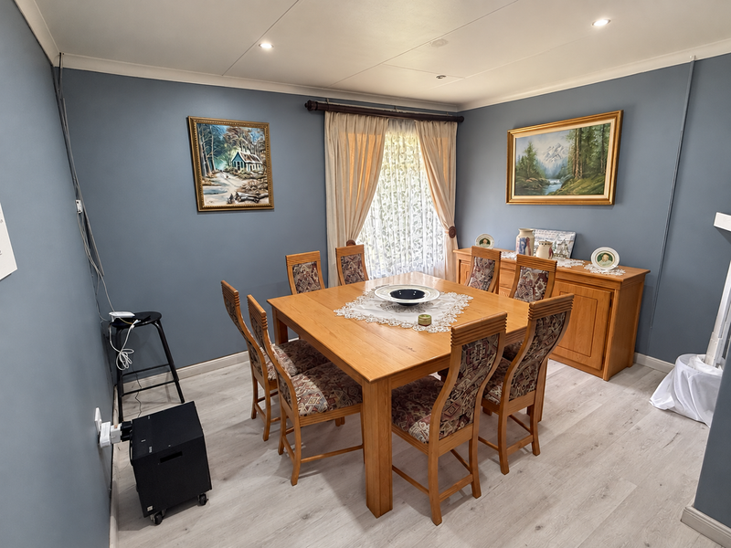 A dining room featuring laminate flooring, recessed downlighting, and blue-painted walls. The space includes a window with curtains and visible surface-mounted electrical wiring.