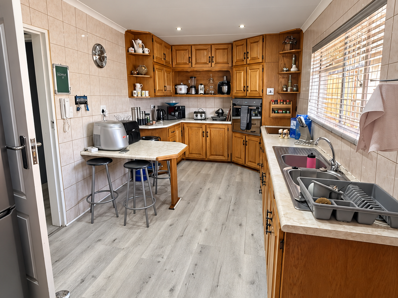 A functional kitchen featuring wooden cabinetry, laminate countertops, a double stainless steel sink, and modern vinyl flooring with recessed lighting.