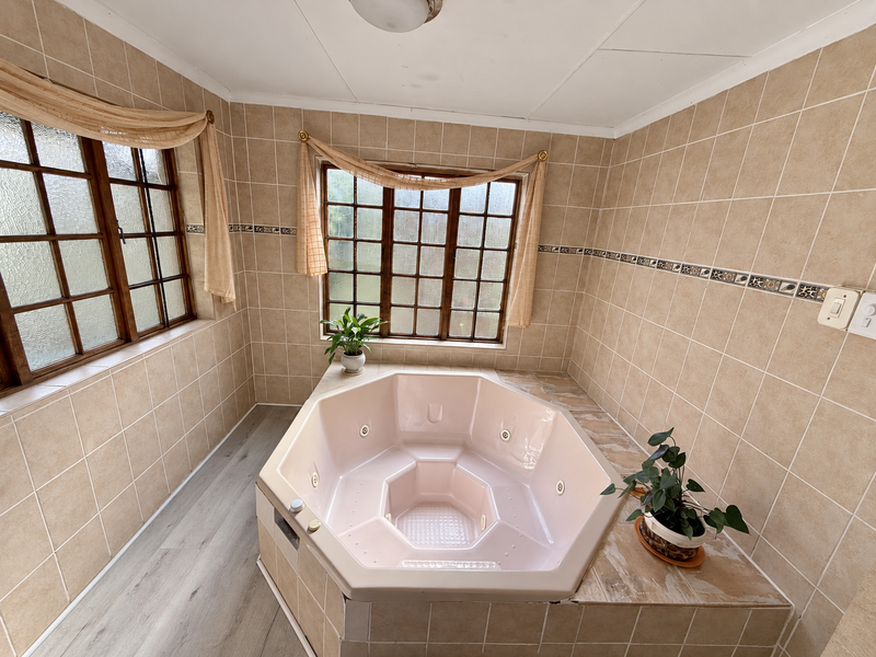 A bathroom featuring a built-in corner spa bath, tiled walls, and timber-framed windows, offering a dated aesthetic ready for modernization.