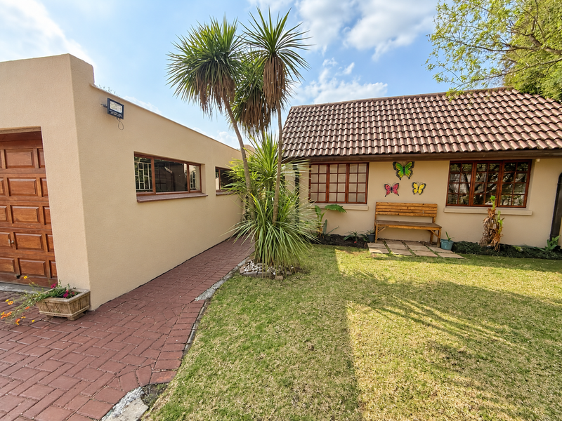 A well-maintained rear exterior view featuring a paved walkway, tiled roof, and established garden area with mature landscaping.