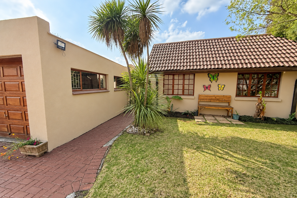 A well-maintained rear exterior view featuring a paved walkway, tiled roof, and established garden area with mature landscaping.