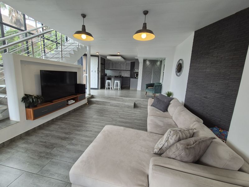 Spacious open-plan living area featuring a modern kitchen, stone-clad feature wall, and a staircase with a stainless steel balustrade.