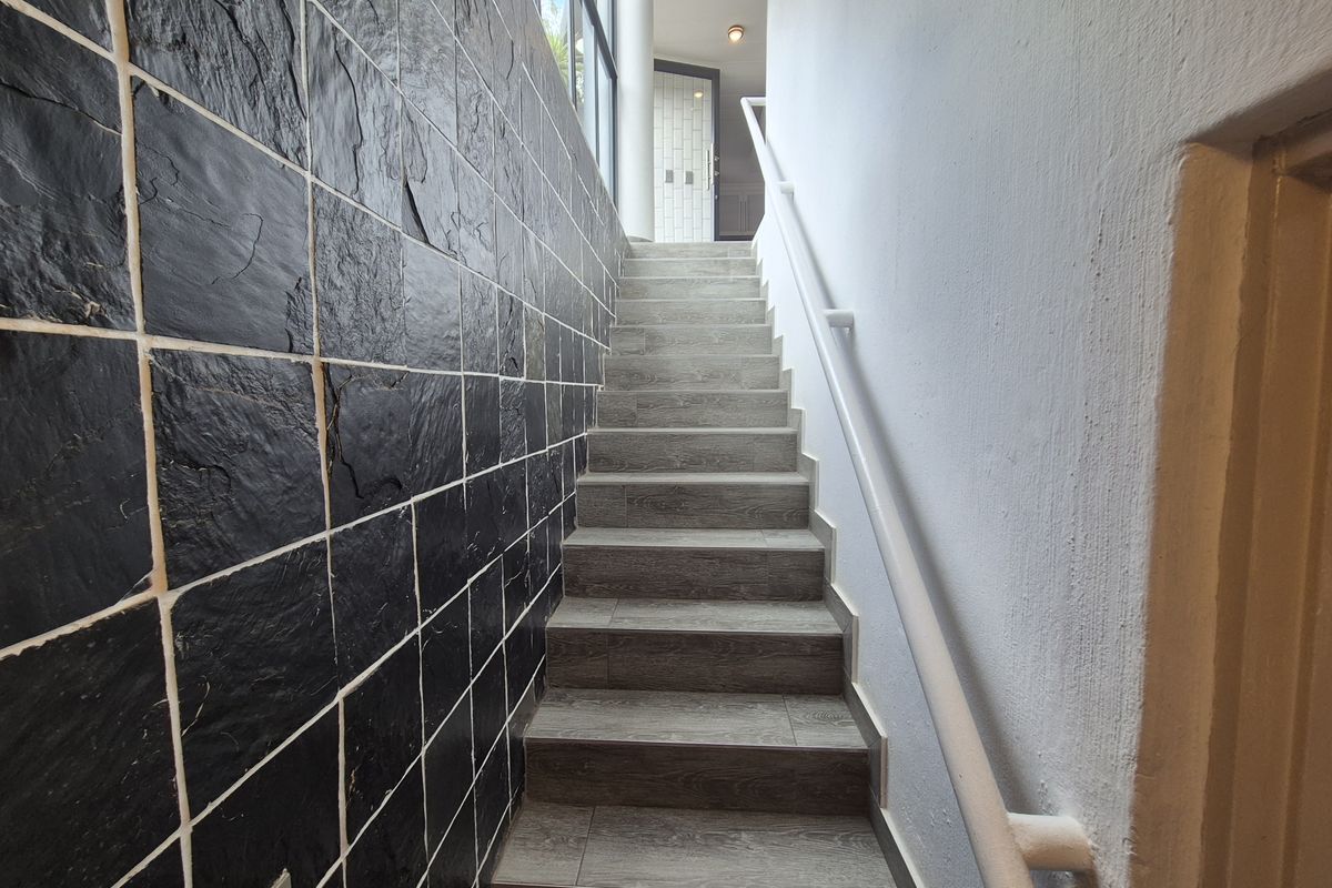A staircase featuring a textured black slate feature wall, wood-look tiled steps, and a white handrail leading to an upper landing.