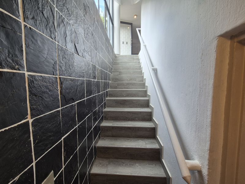 A staircase featuring a textured black slate feature wall, wood-look tiled steps, and a white handrail leading to an upper landing.