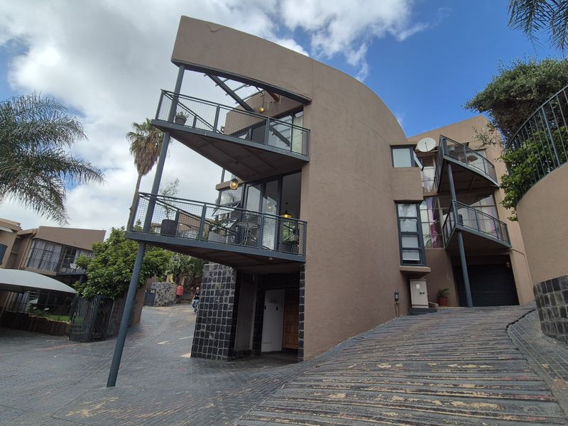 Modern multi-level cluster home featuring unique architectural curves, metal balcony structures, stone accents, and a paved driveway leading to the garage entrance.