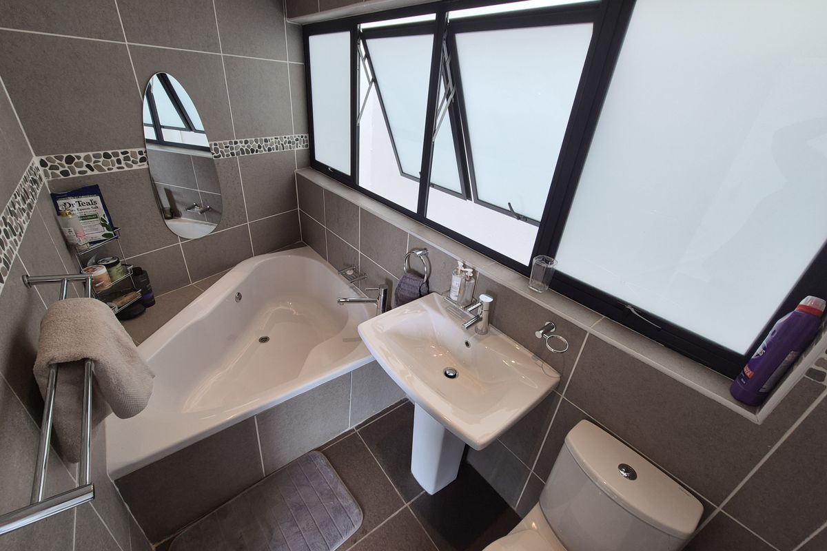 Modern bathroom featuring a corner bathtub, pedestal basin, toilet, and neutral tiled finishes with large windows for natural light.