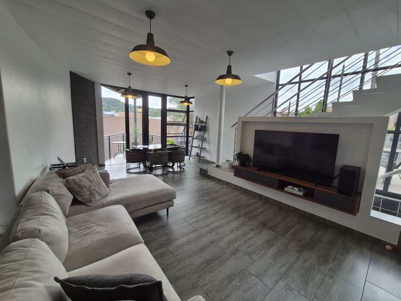 Modern open-plan living area featuring tiled floors, a built-in media console, an accent stone wall, and direct access to a balcony via large glass doors.