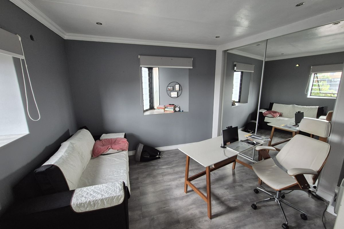 A well-maintained bedroom featuring modern grey walls, laminate flooring, recessed lighting, and large mirrored sliding wardrobe doors.