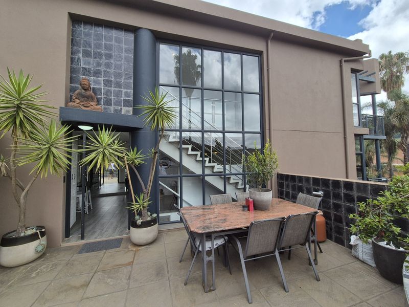 A modern outdoor patio area featuring large steel-framed windows, a staircase, and stylish black tiled accents, perfect for outdoor dining and entertaining.