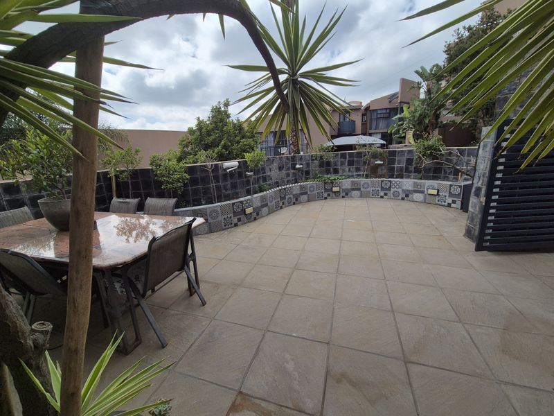 A spacious outdoor patio area featuring large format floor tiles and a curved, decorative tiled retaining wall with integrated lighting.