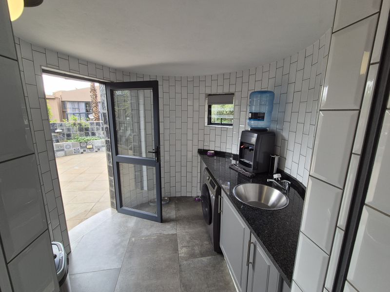 A modern laundry room featuring subway tile walls, granite countertops, a stainless steel sink, and direct access to an outdoor patio area.