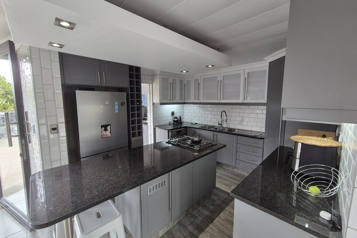 Modern kitchen featuring granite countertops, a central island with a gas hob, subway tile backsplash, and ample grey cabinetry with recessed lighting.