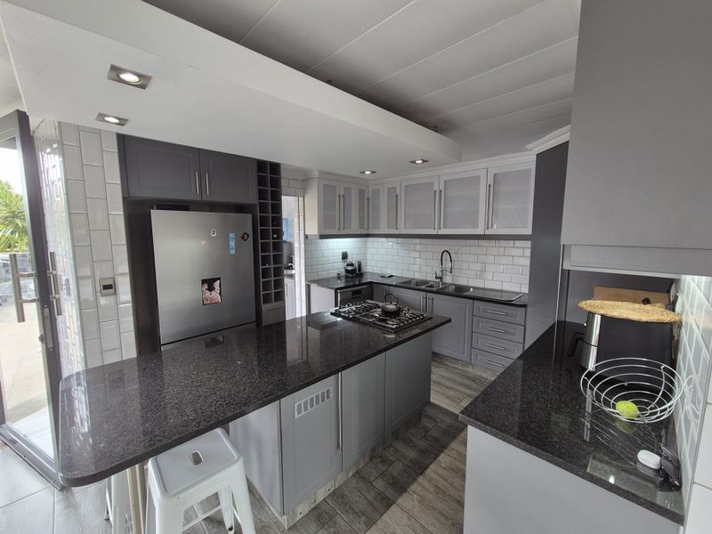 Modern kitchen featuring granite countertops, a central island with a gas hob, subway tile backsplash, and ample grey cabinetry with recessed lighting.
