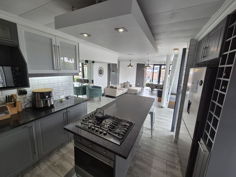 Modern open-plan kitchen featuring a central island with gas hob, granite countertops, subway tile backsplash, and integrated wine storage, flowing into the living area.
