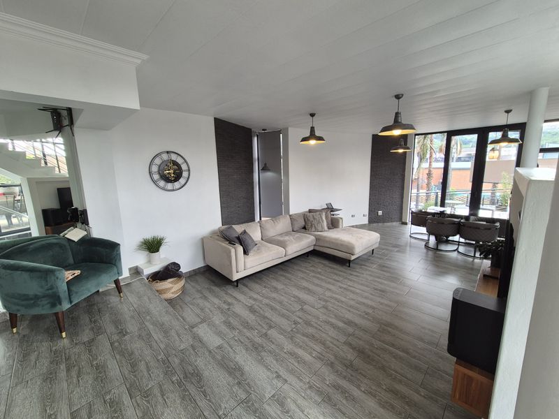 Spacious open-plan living and dining area featuring wood-look tile flooring, modern pendant lighting, and large glass doors leading to an outdoor space.