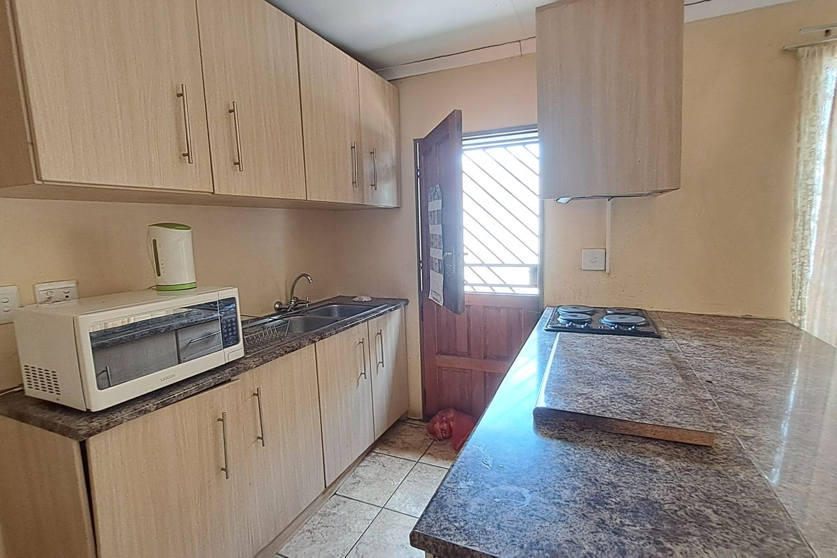 A functional kitchen featuring laminate cabinetry, granite countertops, an electric hob with extractor fan, and direct access to the exterior via a security gate.
