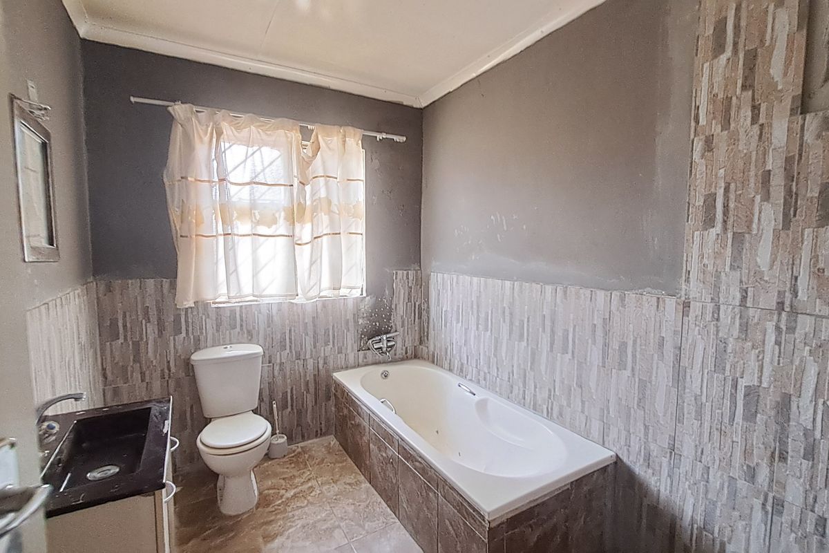 A bathroom featuring a built-in bathtub, toilet, and vanity basin with partially tiled walls and unfinished paintwork.