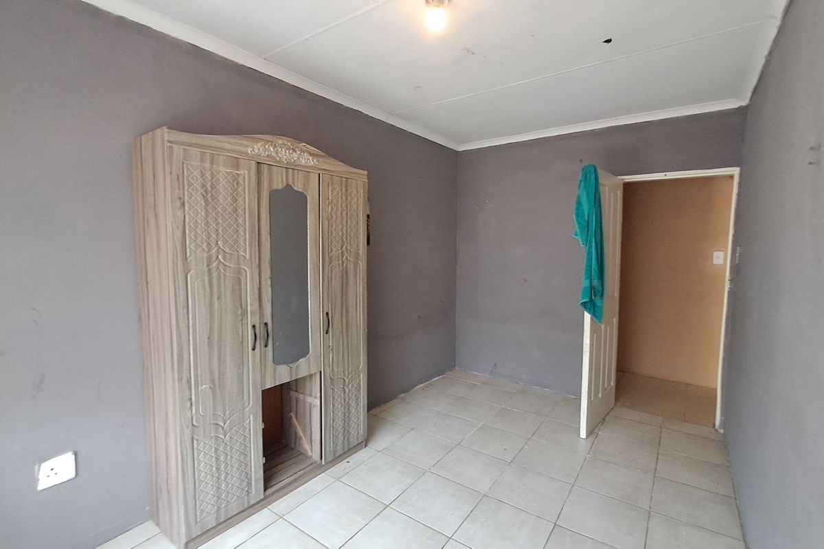 A bedroom featuring tiled flooring and grey painted walls, requiring minor cosmetic updates to improve the overall finish.