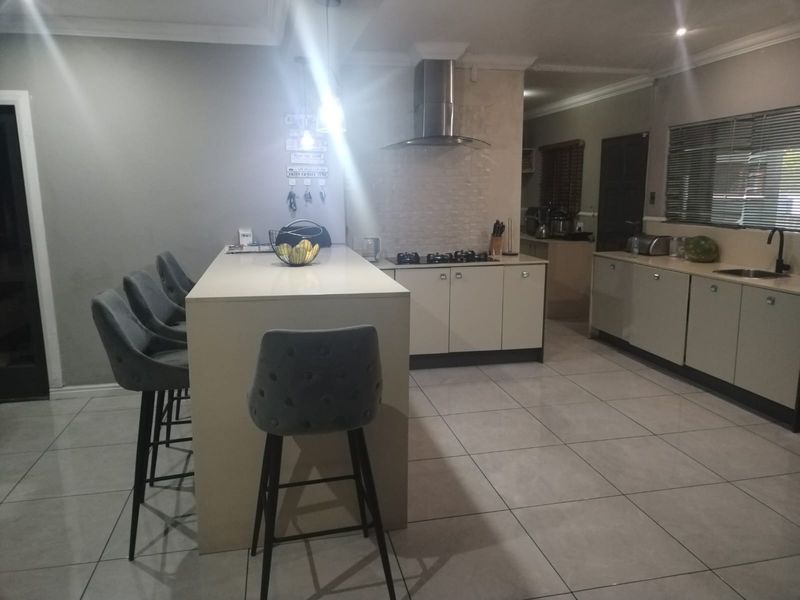 Modern kitchen featuring a central island with breakfast bar seating, gas hob, stainless steel extractor fan, and ample built-in cabinetry with tiled flooring.