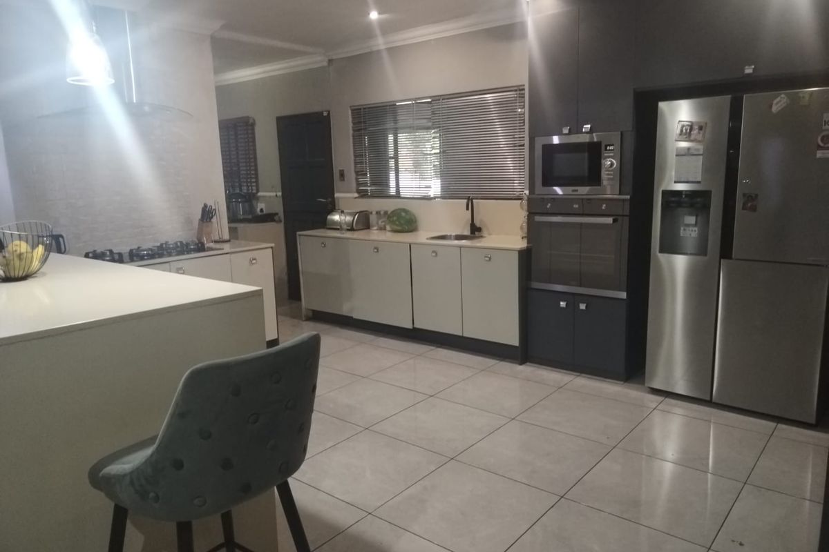 Modern kitchen featuring a central island, built-in oven and microwave, gas hob with extractor, and ample cabinetry with tiled flooring.