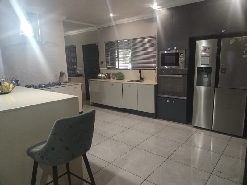 Modern kitchen featuring a central island, built-in oven and microwave, gas hob with extractor, and ample cabinetry with tiled flooring.