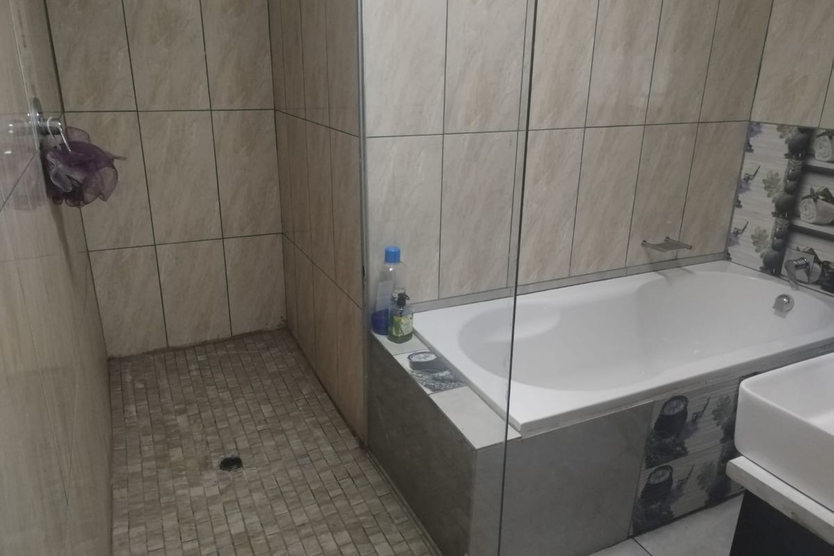 A functional bathroom featuring a walk-in shower, a built-in bathtub with glass screen, and neutral wall and floor tiling.