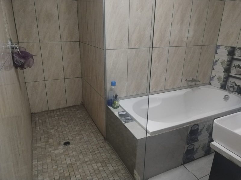 A functional bathroom featuring a walk-in shower, a built-in bathtub with glass screen, and neutral wall and floor tiling.