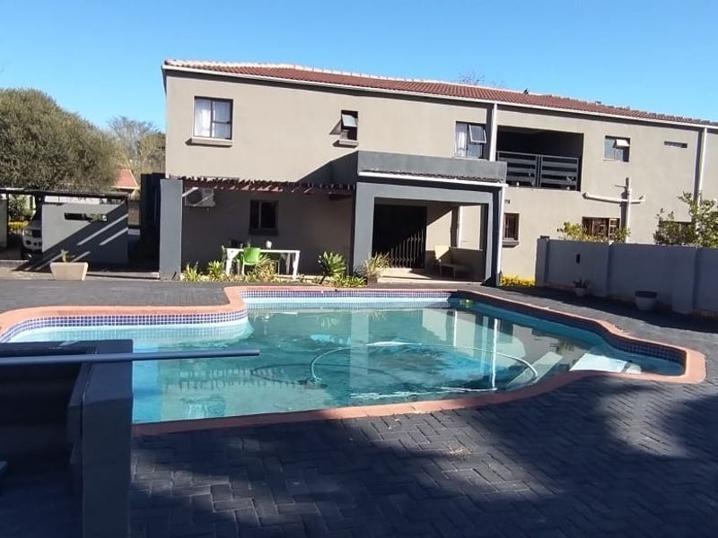 A spacious backyard featuring a swimming pool with a paved deck and a covered patio area attached to the two-story house.