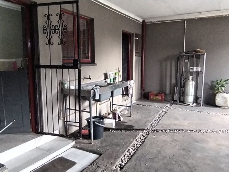 A covered outdoor patio area featuring a stainless steel double sink, concrete flooring with stone detailing, and access to the main dwelling.