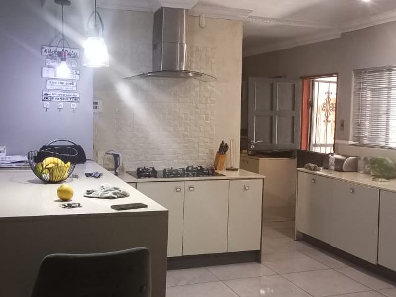 Modern kitchen featuring a central island, gas hob, stainless steel extractor fan, built-in appliances, and tiled flooring with ample cabinetry.