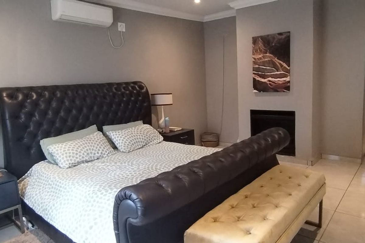 Spacious bedroom featuring tiled flooring, a built-in fireplace, and a wall-mounted air conditioning unit, offering a comfortable and well-maintained living space.