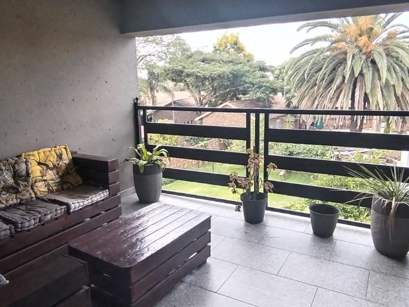 A covered balcony featuring tiled flooring and a black metal balustrade, offering an elevated view of the surrounding garden and neighborhood.