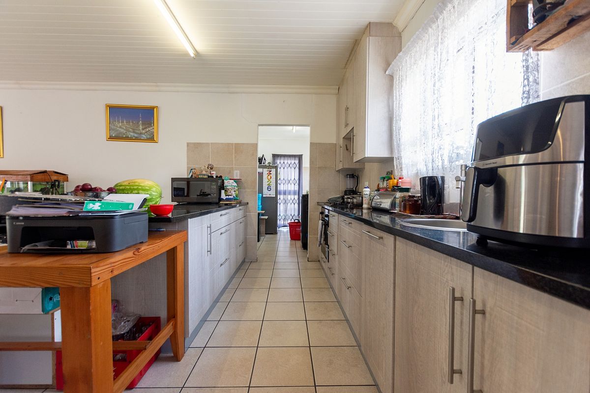 A functional galley-style kitchen featuring dark stone countertops, light wood-grain cabinetry, tiled flooring, and a pass-through leading to an adjacent utility area.