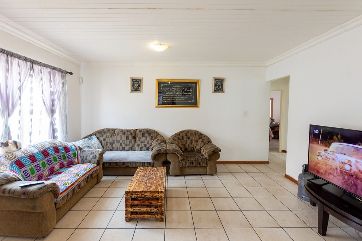 A spacious living room featuring neutral floor tiles, a white tongue-and-groove ceiling, and a doorway leading to an adjacent area.