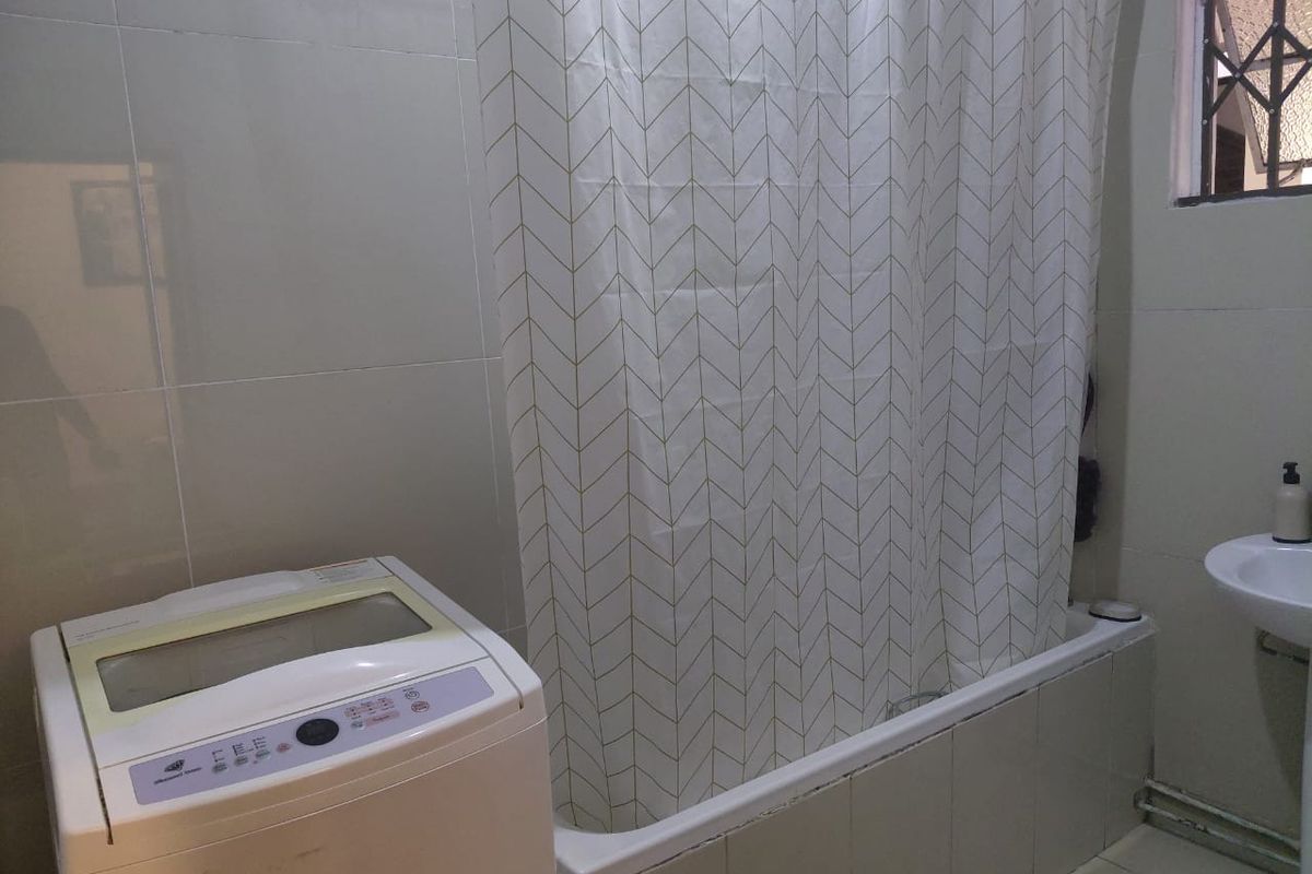 A functional bathroom featuring a bathtub with shower curtain, pedestal basin, and dedicated space for a top-loading washing machine.